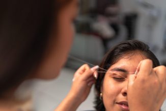 Beautician is shaping eyebrows of a young client with threading technique in a beauty salon